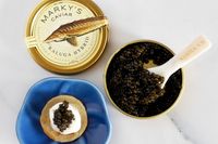 A tin of Marky's kaluga hybrid caviar next to a prepared blini topped with crème fraîche and caviar