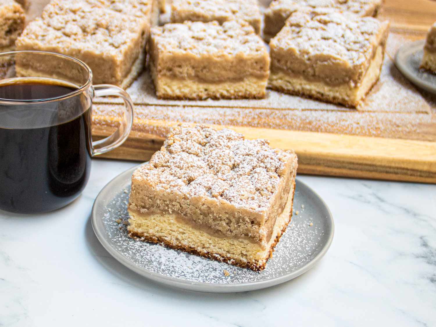 Freshly dusted Crumb bun on a plate with a cup of coffee, and a wooden board of several crumb buns in the background