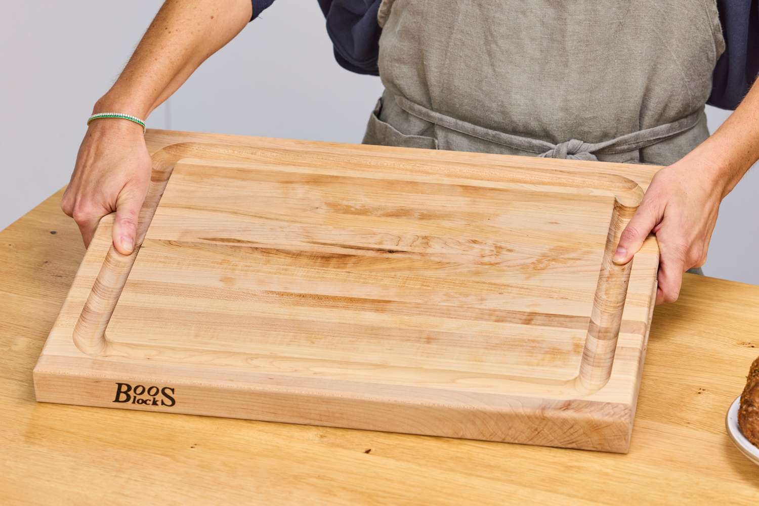 A person holding a John Boos Reversible Maple Wood Cutting Board with Juice Groove