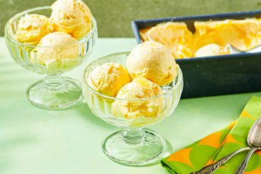Scoops of mango ice cream in glass bowls with an ice cream tub in the background