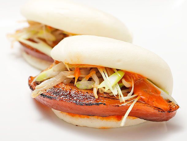 Closeup of a pork belly bun with spicy mayo, scallions, and pickled bean sprouts.