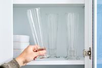 A person placing a pilsner glass onto a kitchen shelf. 