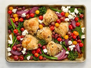 Sheet pan with roasted chicken thighs tomatoes red onions olives broccolini and feta cheese crumbles