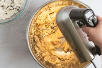 A person using a Breville hand mixer to mix cookie dough.
