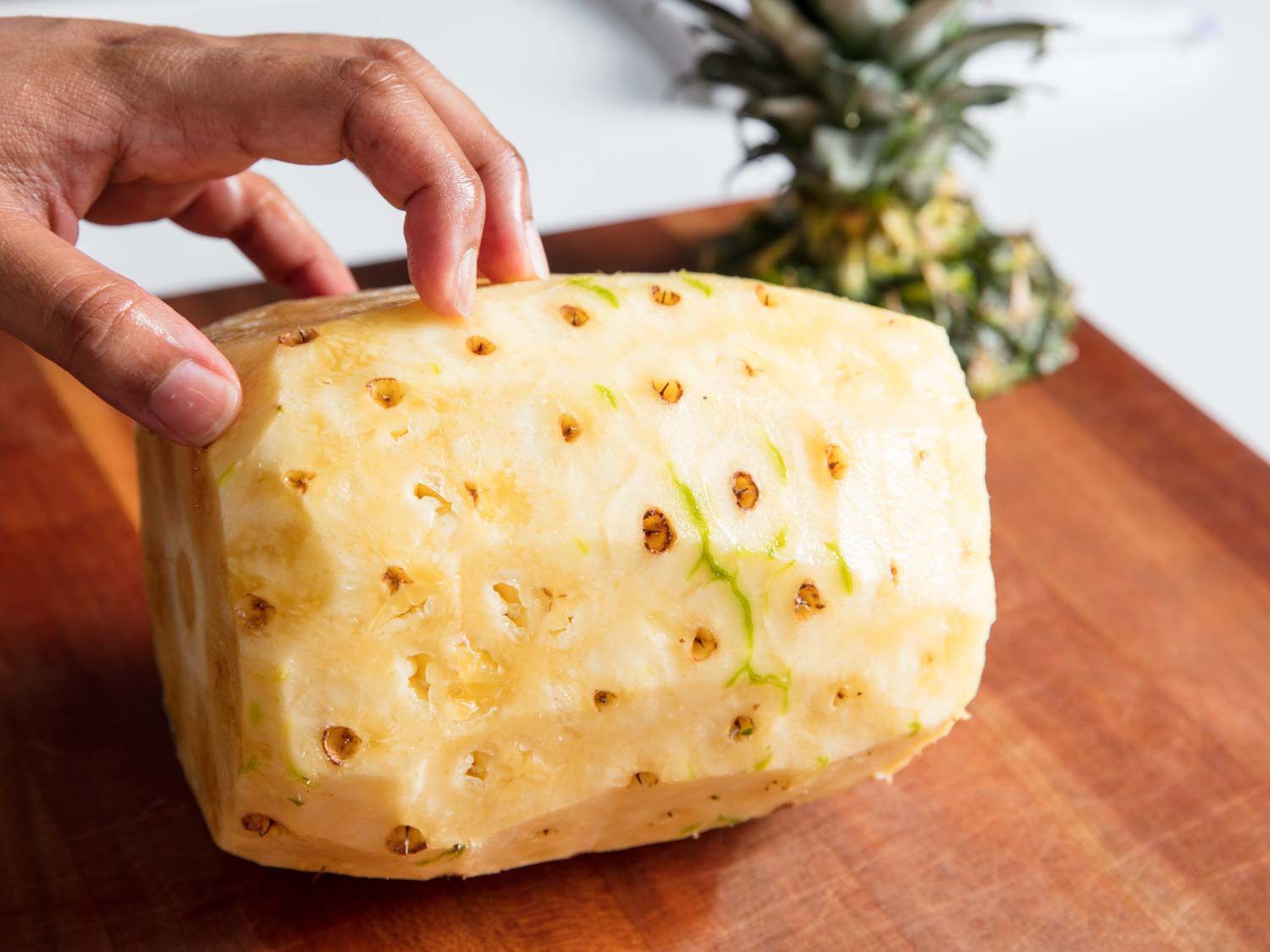 A pineapple with the sides trimmed off on a cutting board.