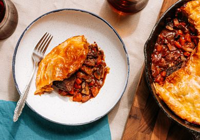 Beef bourguignon pot pie served on a plate with a decorative napkin and a skillet nearby