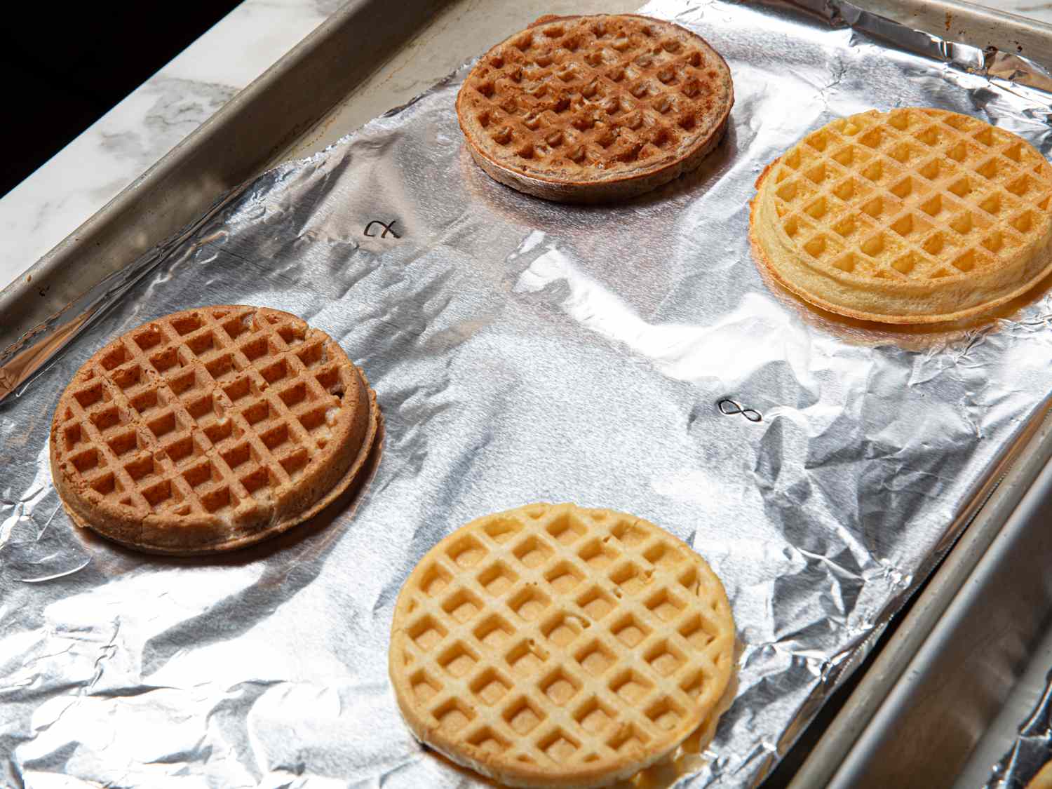 Four waffles on a baking sheet lined with aluminum foil