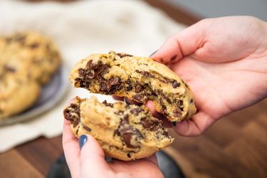 Person breaking open a gooey chocolate chip cookie in their hands