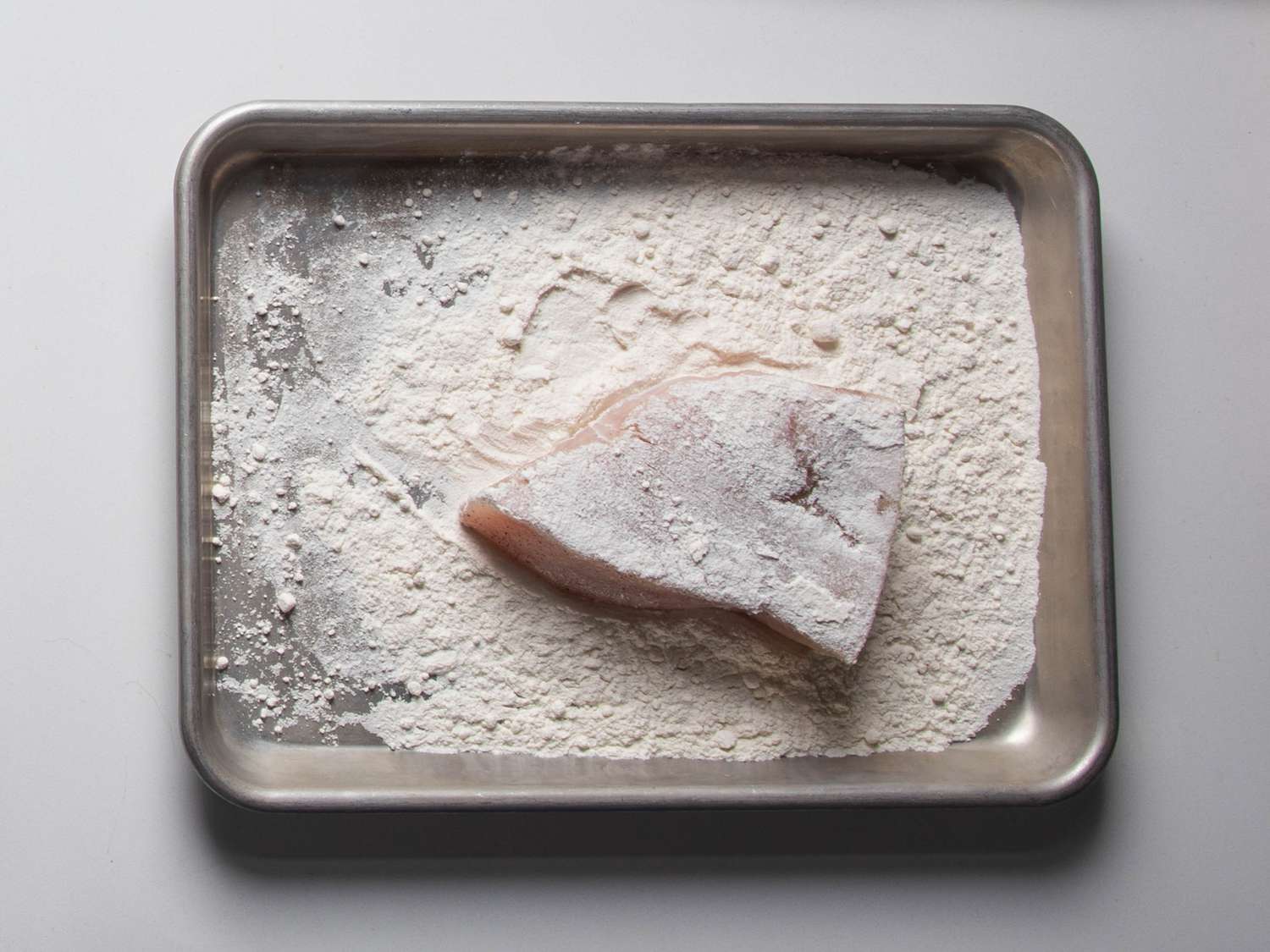 A swordfish steak sits on a small tray after being dredged in flour.