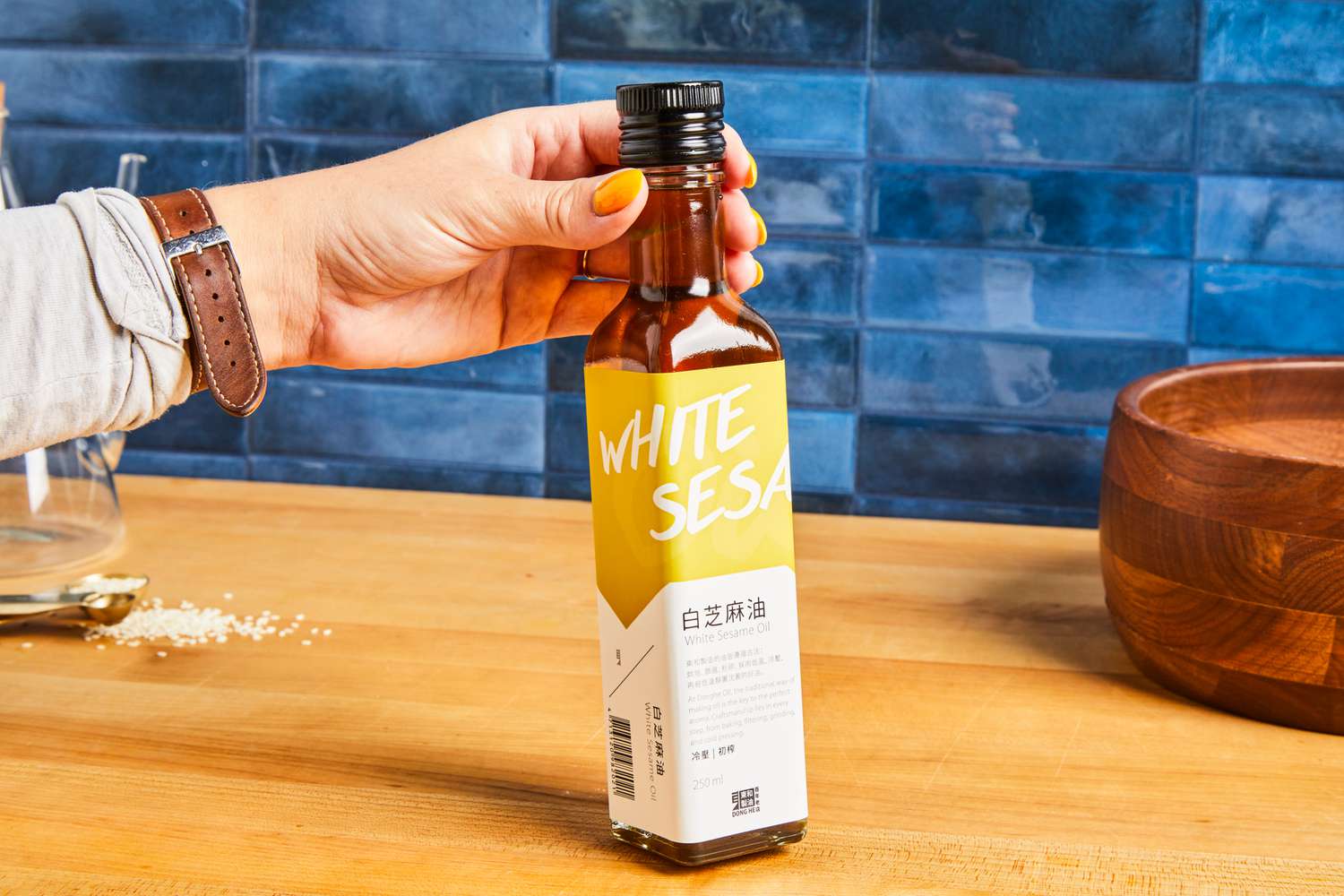 A hand holding a bottle of white sesame oil on a kitchen counter