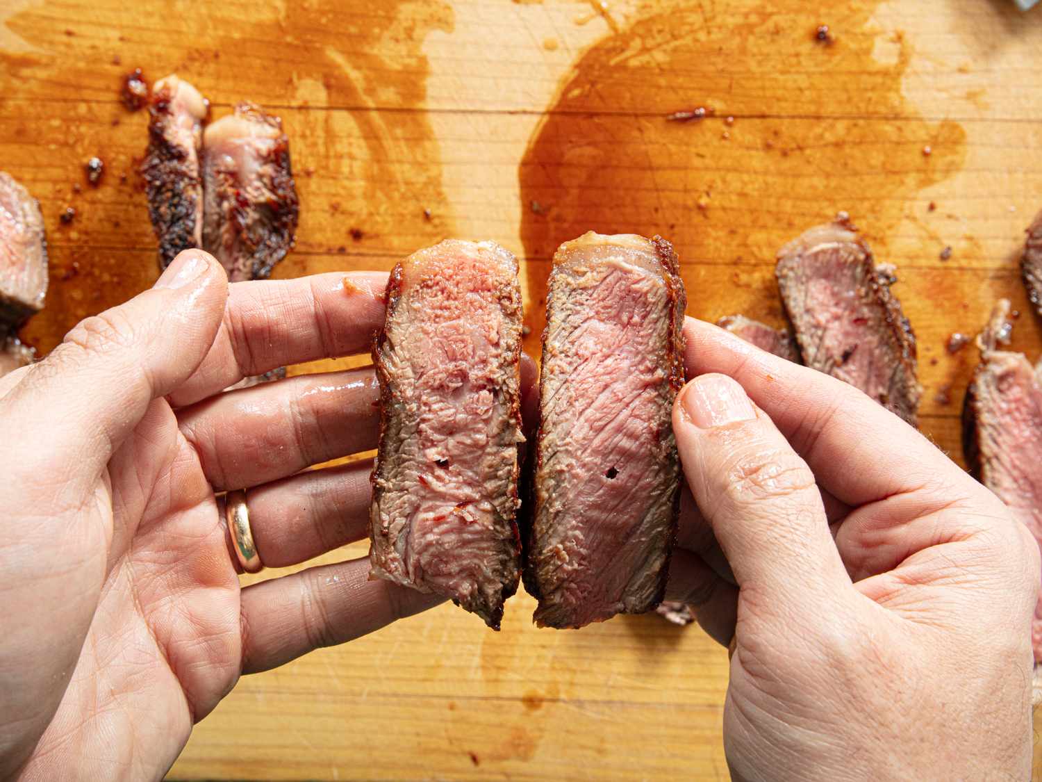 Person holding two pieces of sliced cooked meat with visible pink center
