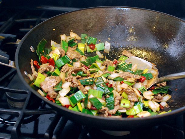 Adding beef back to the wok containing chiles, garlic and leek greens.