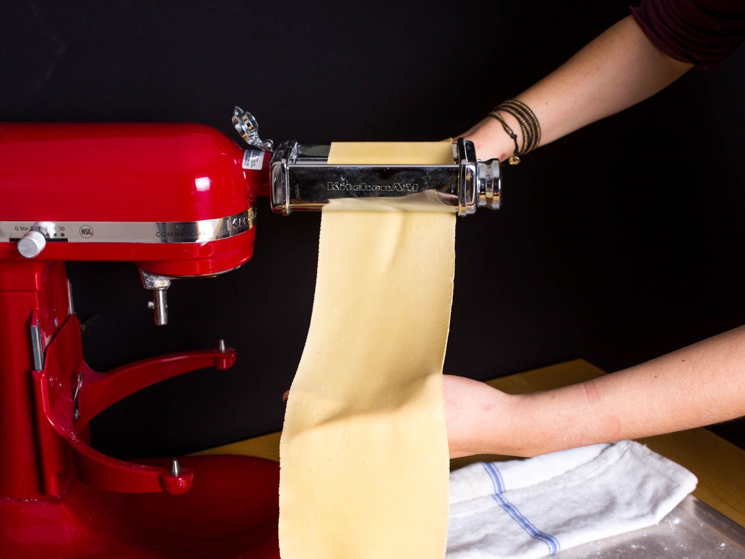 Passing a thin sheet of pasta dough through a pasta-rolling attachment on a stand mixer. 