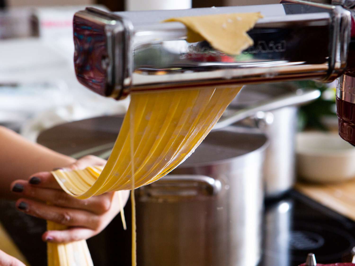 a sheet of pasta being cut into fettucine with the kitchenaid pasta cutter