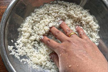A person washing rice in a metal bowl with water