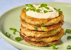stack of boxty pancakes with dollop on sourcream, and garnished with green onions on a green place on stone surface.