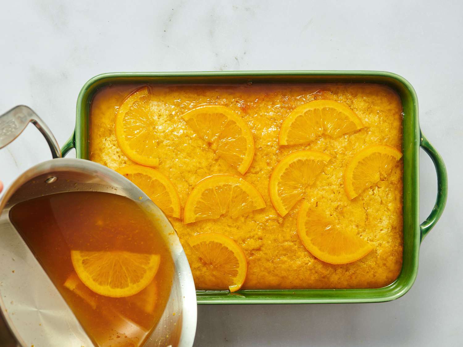 A tray of dessert with orange slices on top, syrup being poured from a pitcher