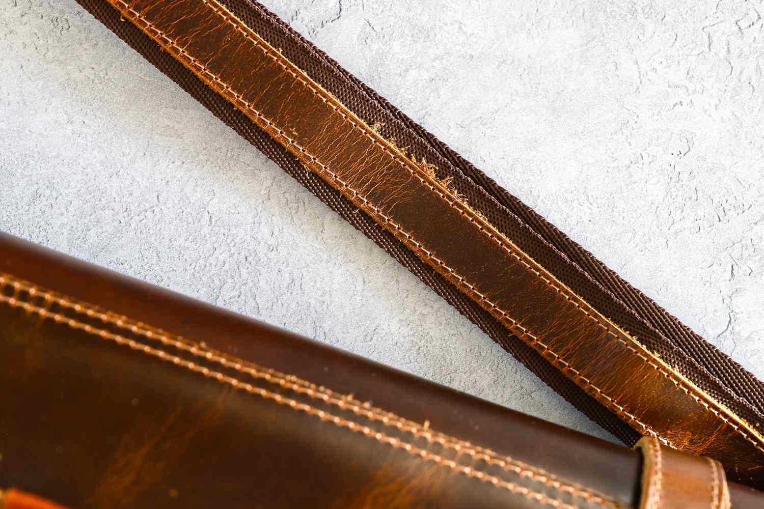 A closeup of a leather strap of Rustic Town Genuine Leather Chef Knife Roll with stitching on a textured background
