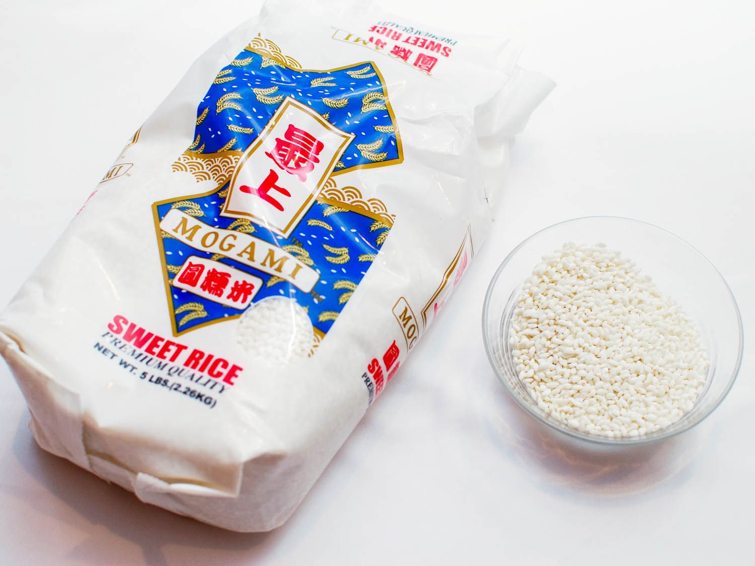 A bag of uncooked sweet sticky rice and a bowl holding the grains of rice on a stone counter.