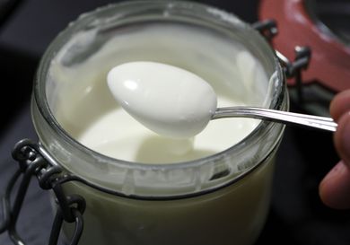 A jar of homemade crème fraîche, with a spoon dipping in it.