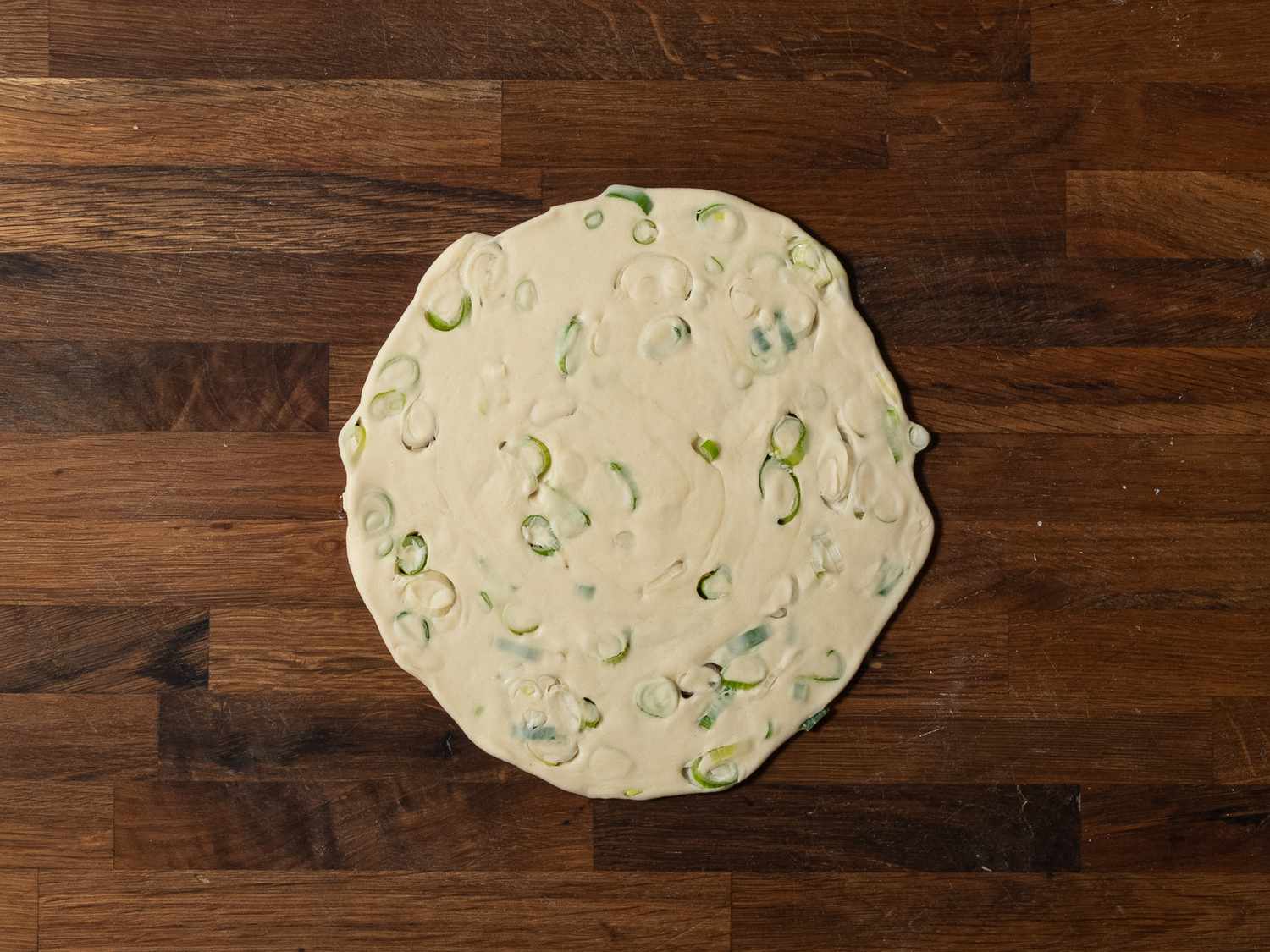 An overhead shot of the scallion pancake on a wooden cutting board, prior to being fried.