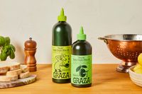 Two bottles of Graza extra virgin olive oil labeled Sizzle for cooking and Drizzle for finishing placed on a kitchen counter