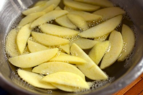 Air bubbles surfacing in bowl of apple slices soaking in hot water.