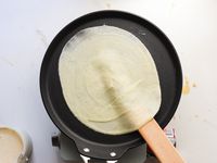 A spatula being used to flip a crepe.