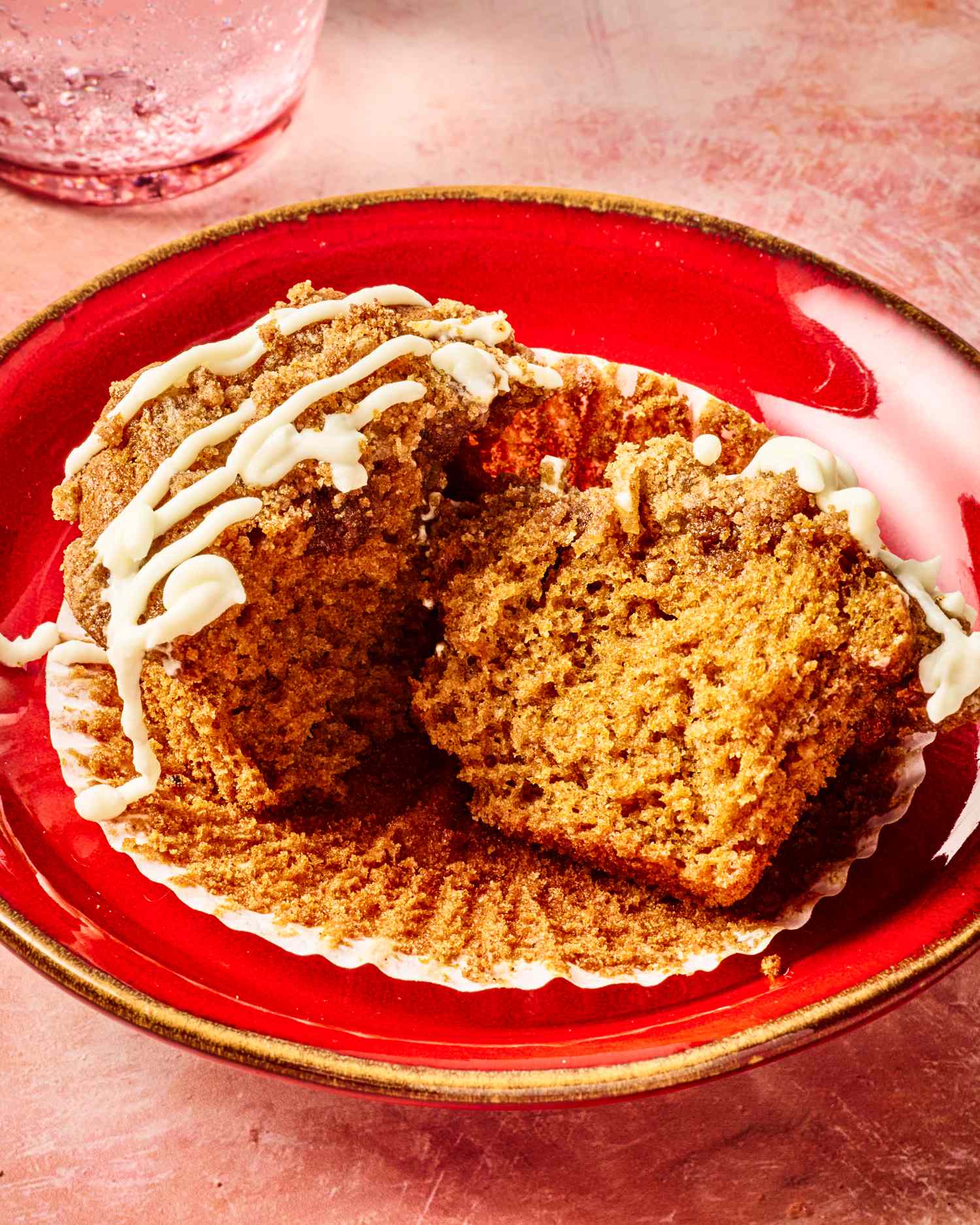 A broken gingerbread muffin with white icing served on a red plate with a cupcake wrapper