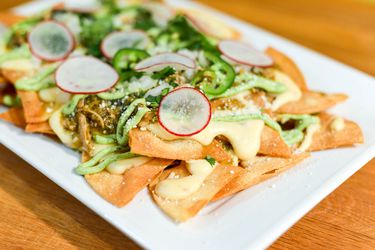 A plate of tortilla chips topped with chile verde, chicken, sliced radish, and jalapeño slices