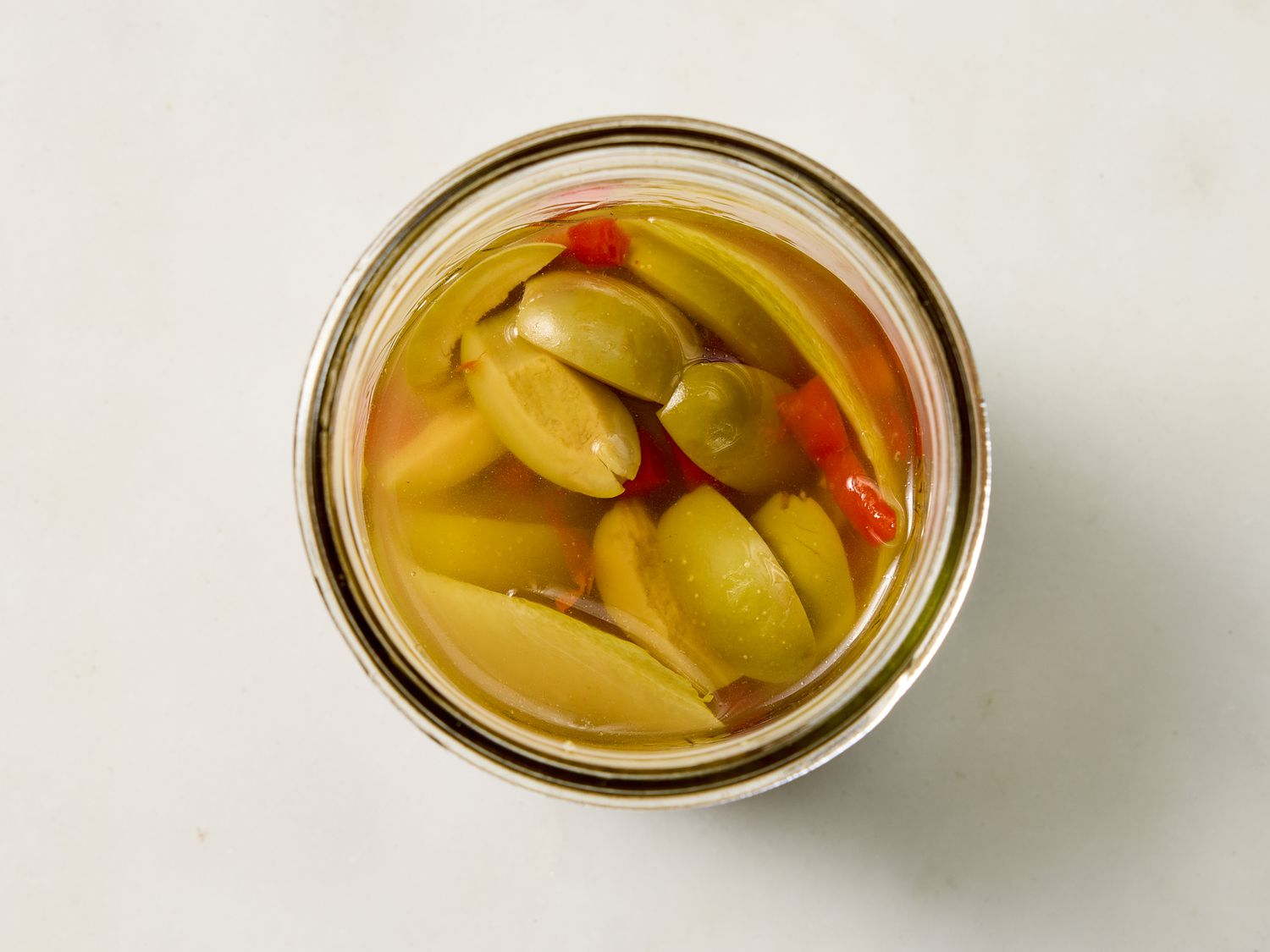 A top view of a jar containing olives and red pimento slices submerged in liquid