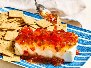 Cream cheese topped with pepper jelly, served on a plate with crackers