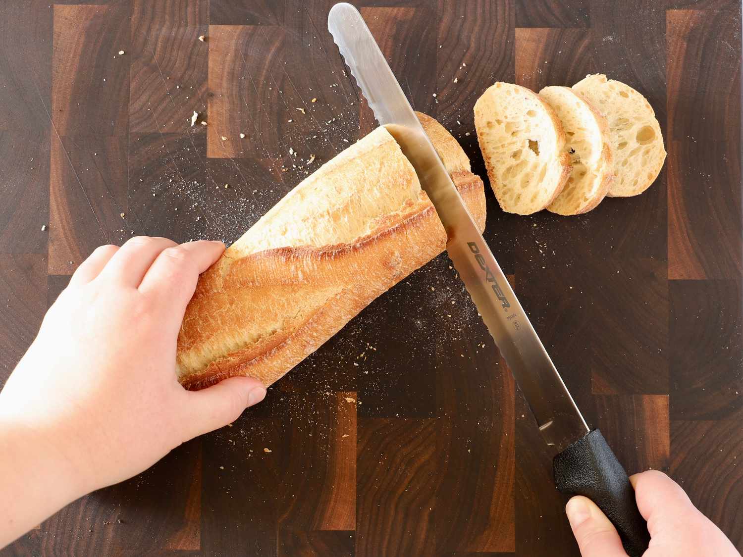 A bread knife slicing a baguette into slices