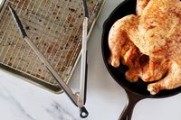 The OXO 12-Inch Silicone Tongs sitting on a baking sheet next to a chicken