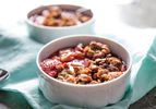 Two bowls of strawberry-rhubarb crisp, served on a light blue cloth.