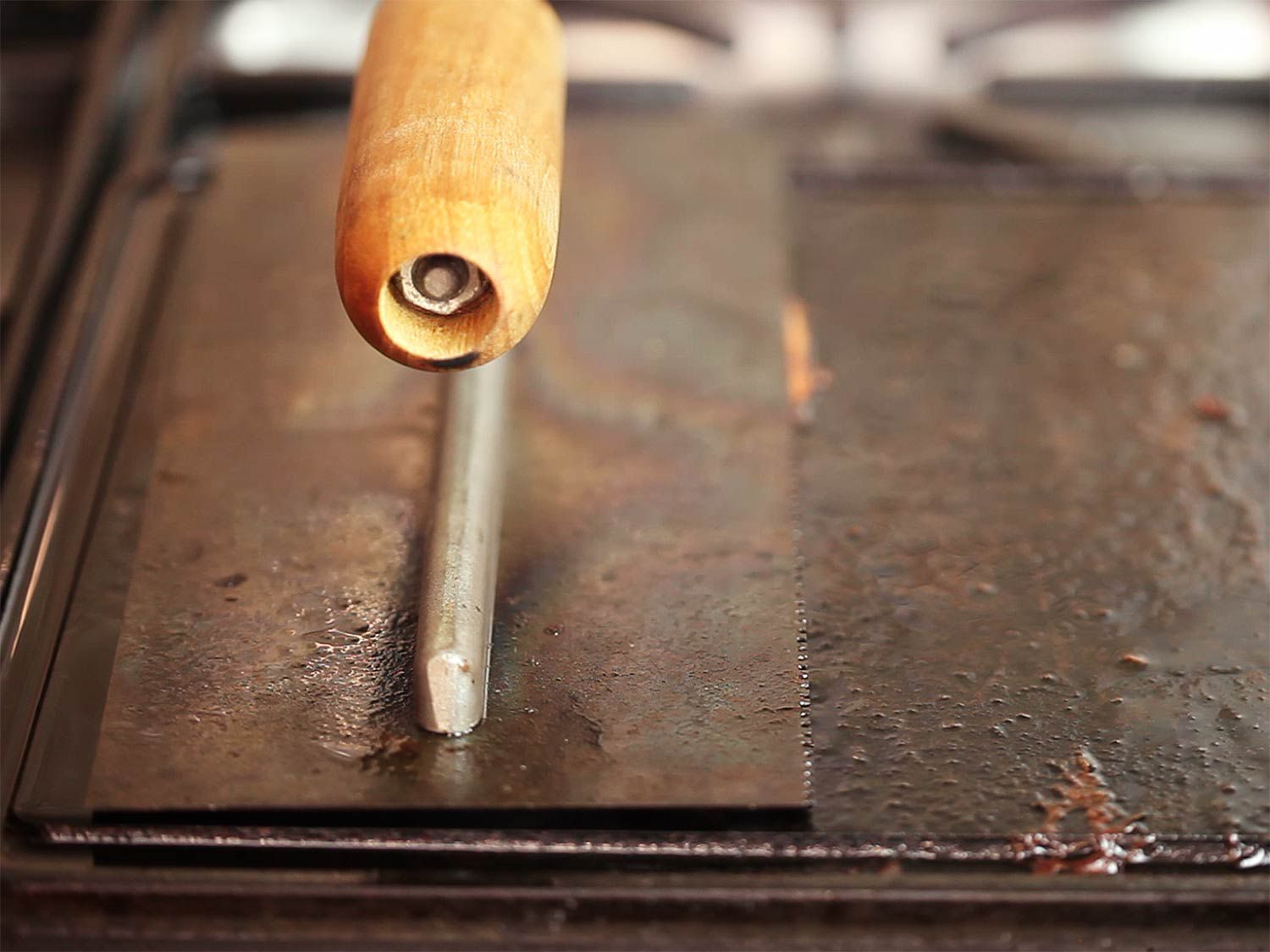 A heavy construction trowel pressing down on strips of bacon on a griddle.