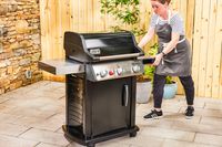 A person wheels the Weber Spirit EX-325s Smart Grill across a patio