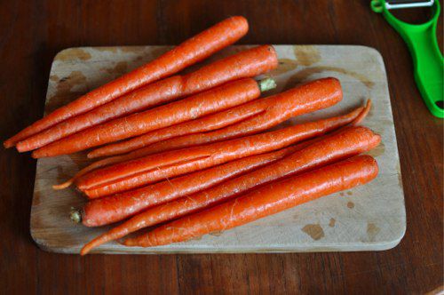 Washed carrots piled on a cutting board, ready to be peeled.