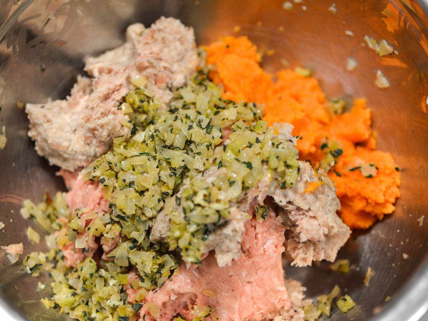 Veggie herb mix, mashed sweet potato, pork sausage, and ground turkey in a mixing bowl.