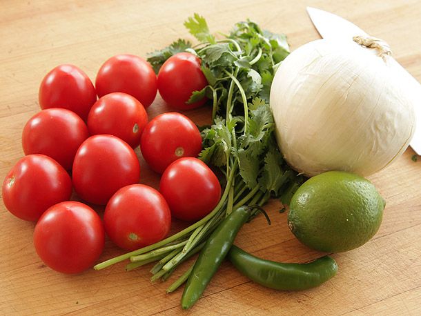 Ripe tomatoes, bunch of cilantro, green pepper, lime, and white onion on wooden surface