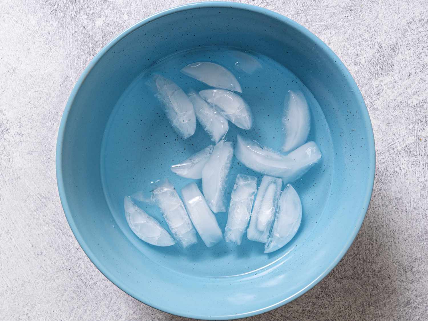A blue bowl filled with water and ice cubes, making a water bath that will be used to cool down the hot, cooked eggs.