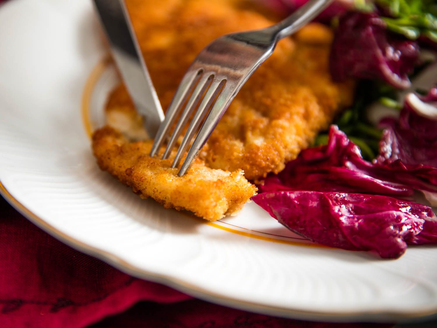 Close-up of a chicken cutlet being cut with a knife and fork.
