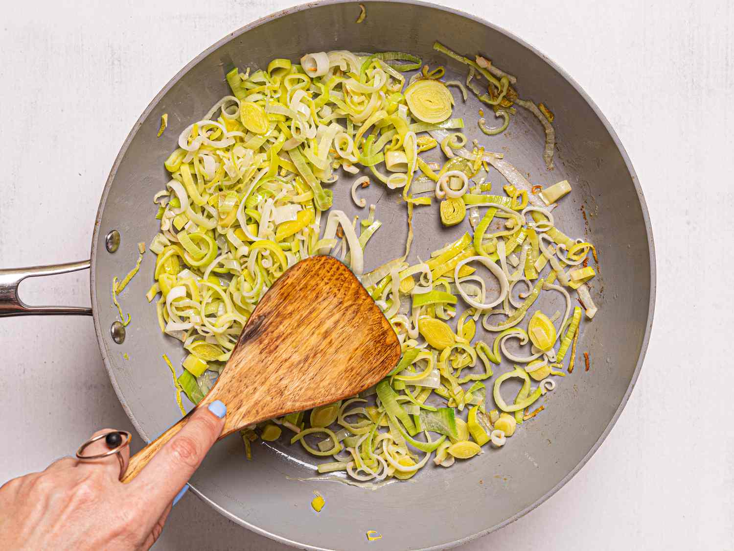 Sautéing sliced leeks in a pan with a wooden spatula.