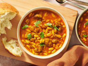2 bowls of Loubia Stew on a wooden board with bread on the side and fabric napkin on the bottom of photo