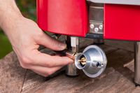 A hand pulling the propane hose from Cuisinart CGG-750 Venture Gas Grill