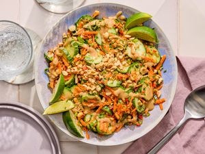 Plate of cucumber salad garnished with crushed peanuts and lime wedges on a table set with dining utensils
