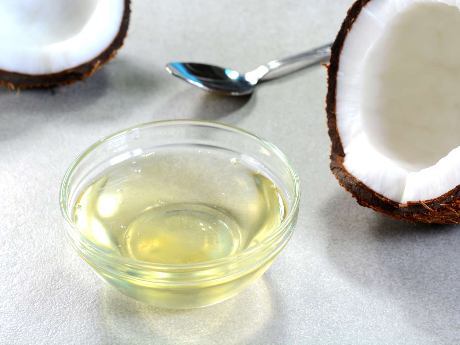 A bowl of coconut oil with halved coconuts and a spoon on a surface