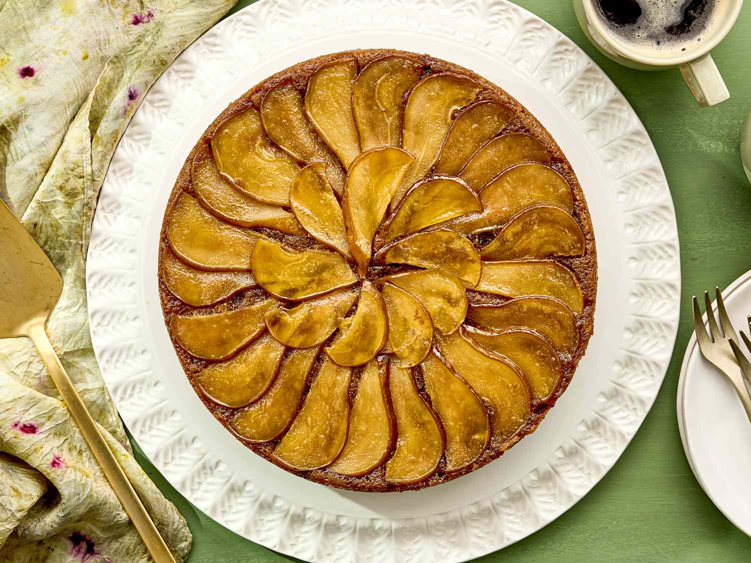 Upsidedown pear cake arranged on a white plate accompanied by tableware and a cup of coffee