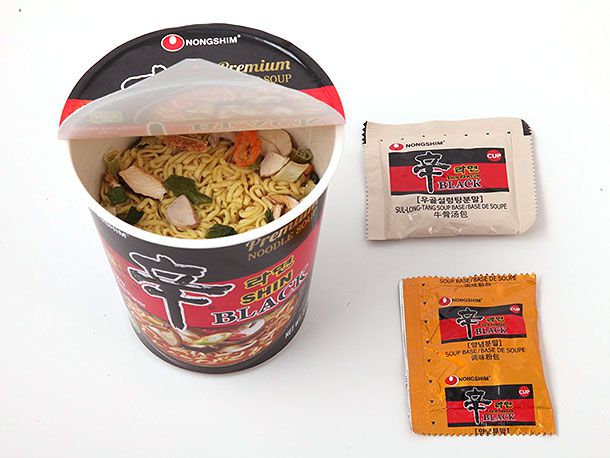 An open cup of premium Shin Black ramen and its two flavoring packets.