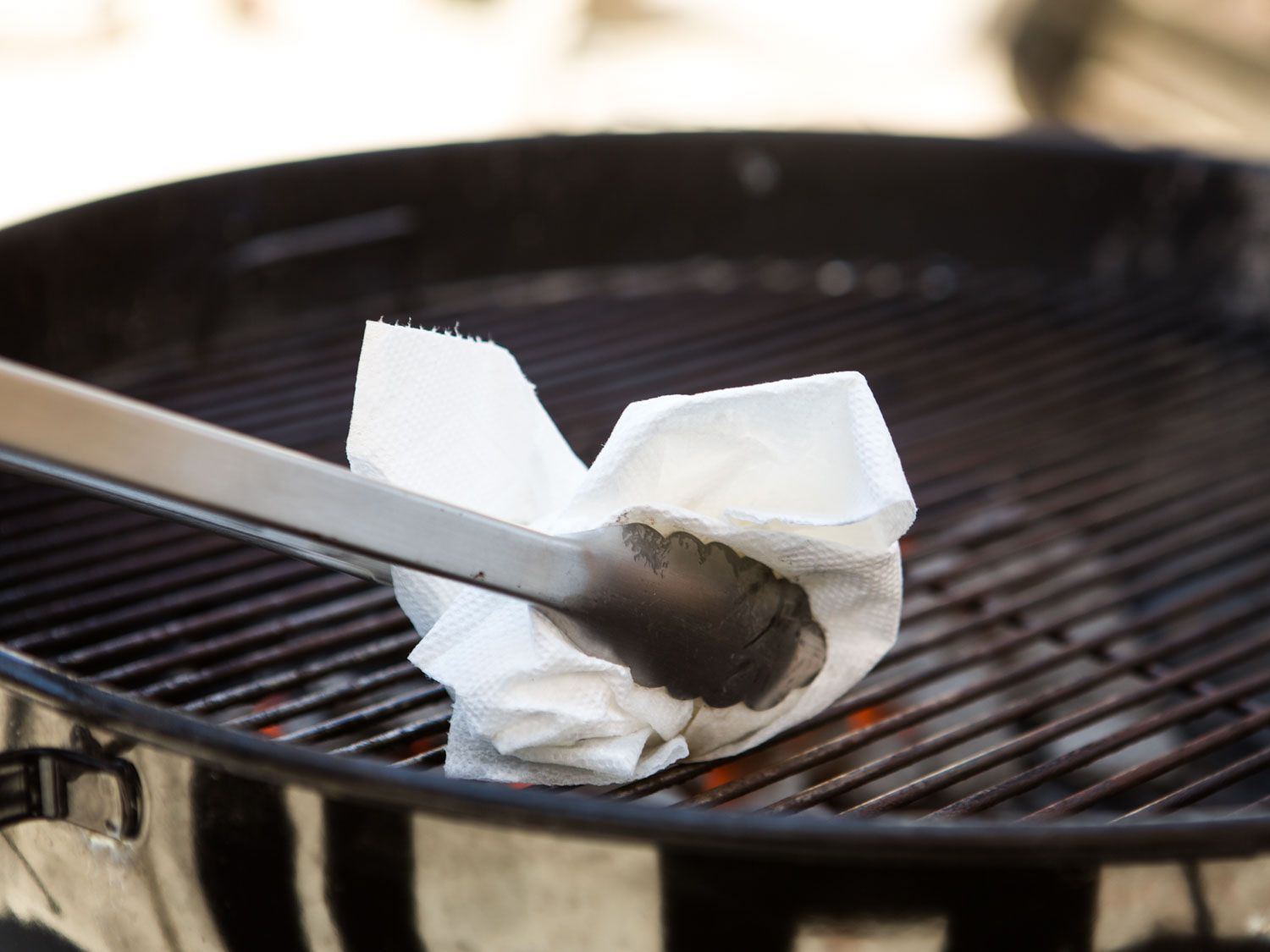 Using an oiled paper towel and tongs to oil grill grates.